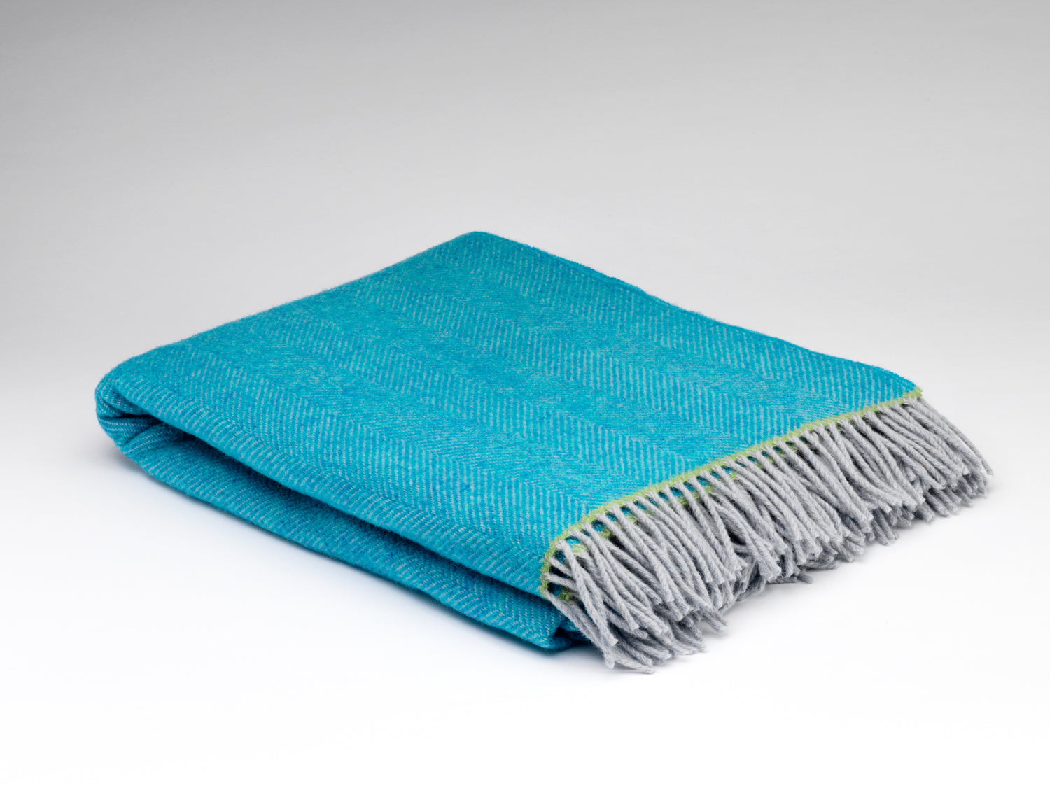 Folded teal blanket with gray fringe on a white background
