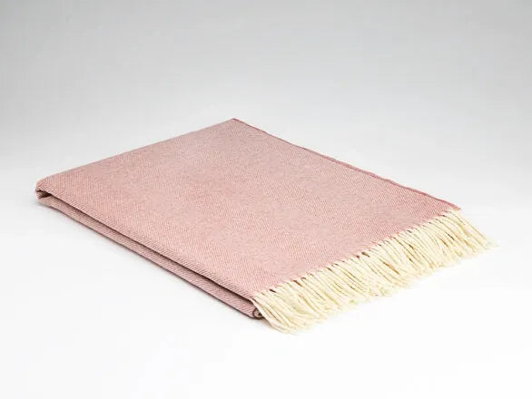 Pink throw blanket with beige fringe on a light gray background