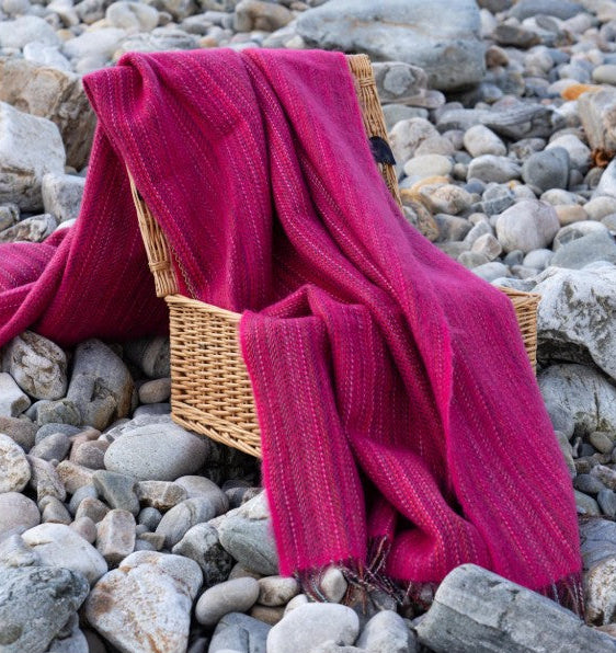fushia blanket draped over a wicker basket on pebbles