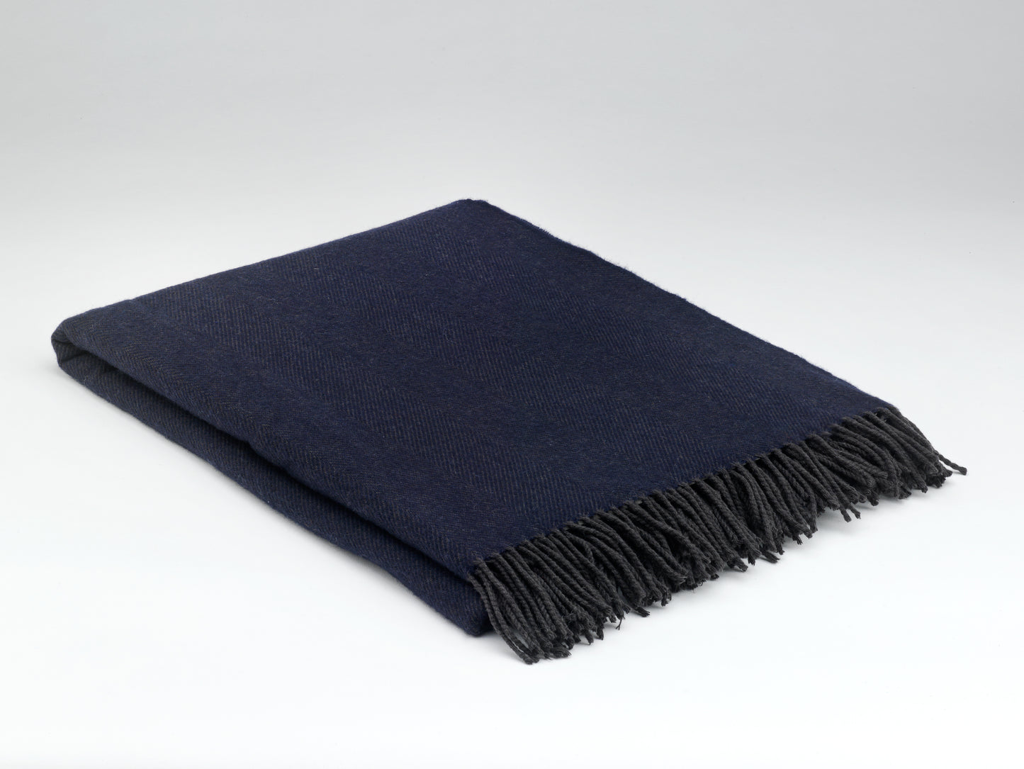 Navy blue throw blanket with fringes on a light gray background