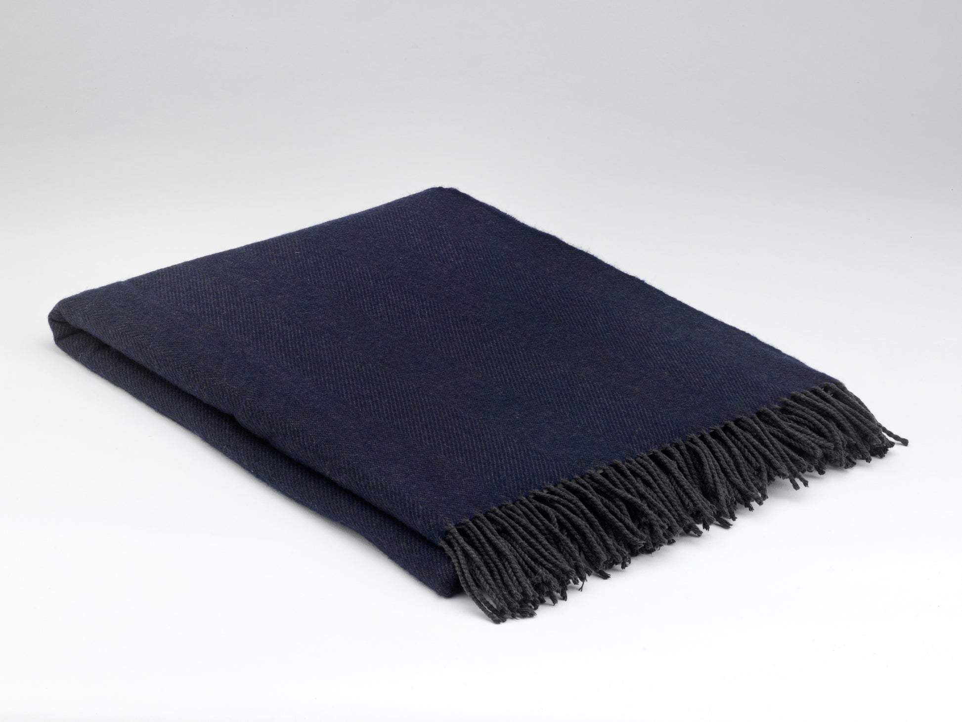 Navy blue throw blanket with fringes on a light gray background