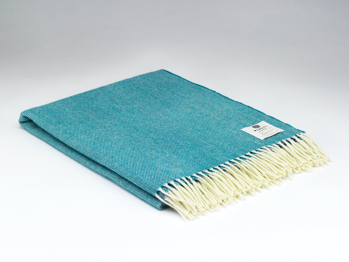 Teal throw blanket with white fringe on a light gray background
