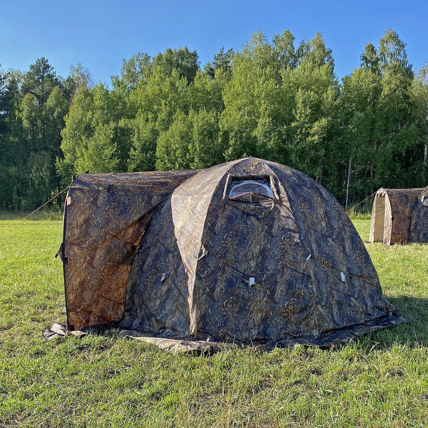 Camouflage bereg hot tent in a grassy field with trees in the background