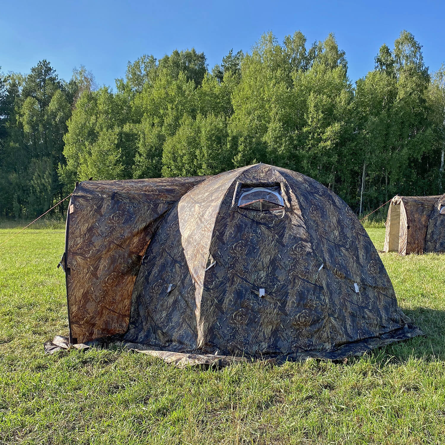 Camouflage bereg hot tent in a grassy field with trees in the background
