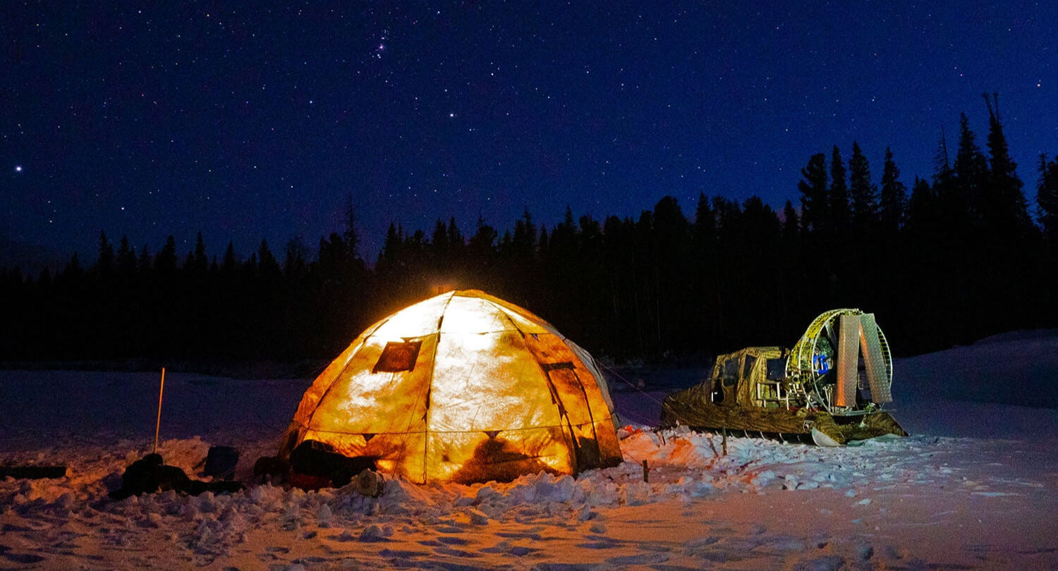Two illuminated tents in a snowy landscape under a starry night sky.